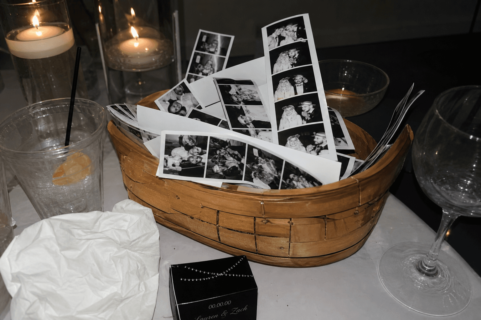 A basket of wedding photo booth strips sitting on a reception table, some strips left uncollected by guests who moved on to dinner