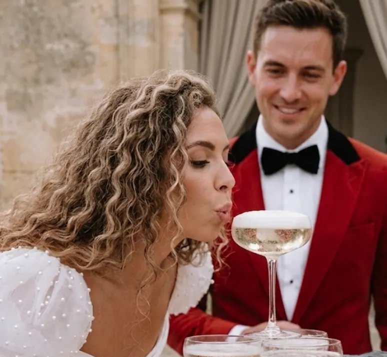 Bride blowing champagne foam while the groom laughs at a playful reception moment