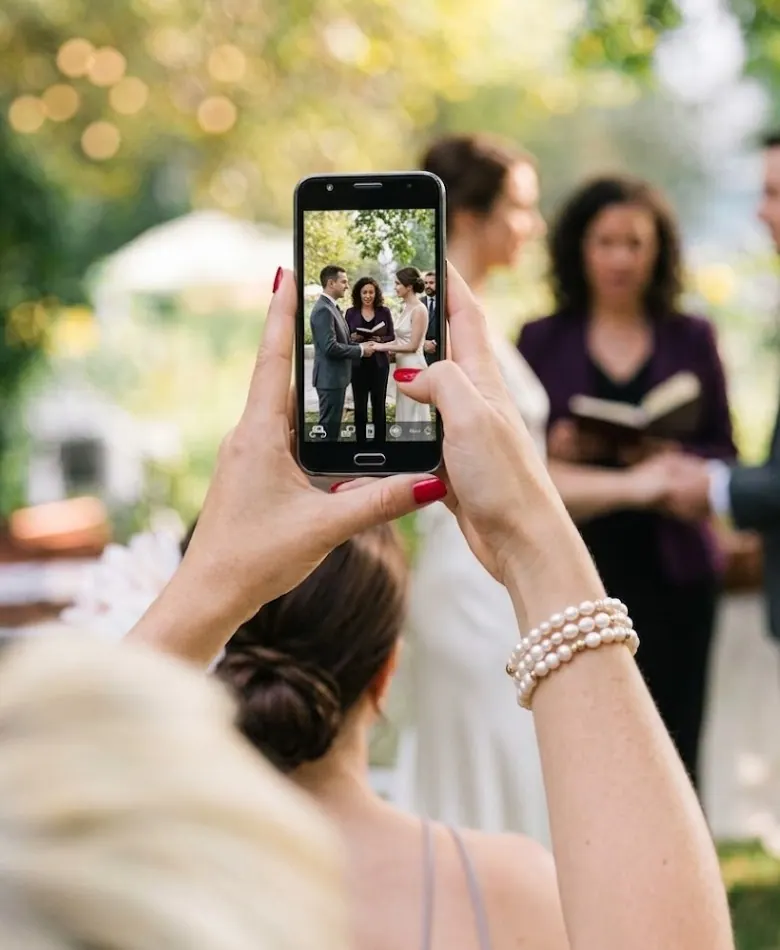 Wedding guest holding a smartphone to photograph the outdoor ceremony