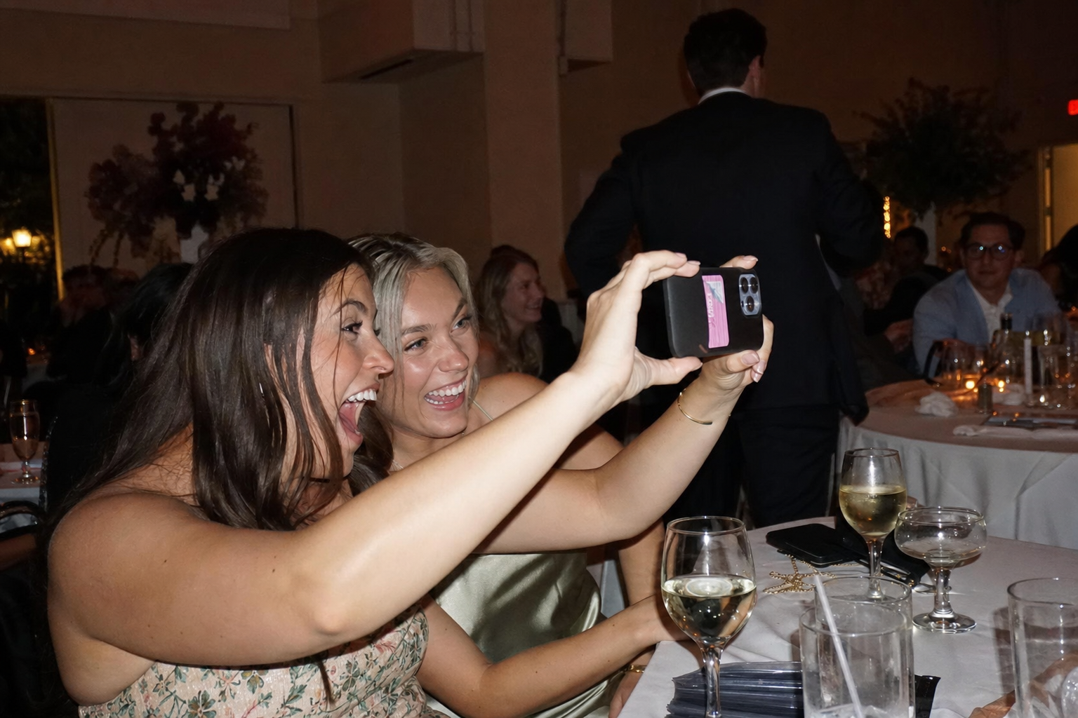 Guests capturing candid reception moments on their phones during dinner Wedding guests laughing and taking photos on their phones at a reception table, capturing candid moments during dinner