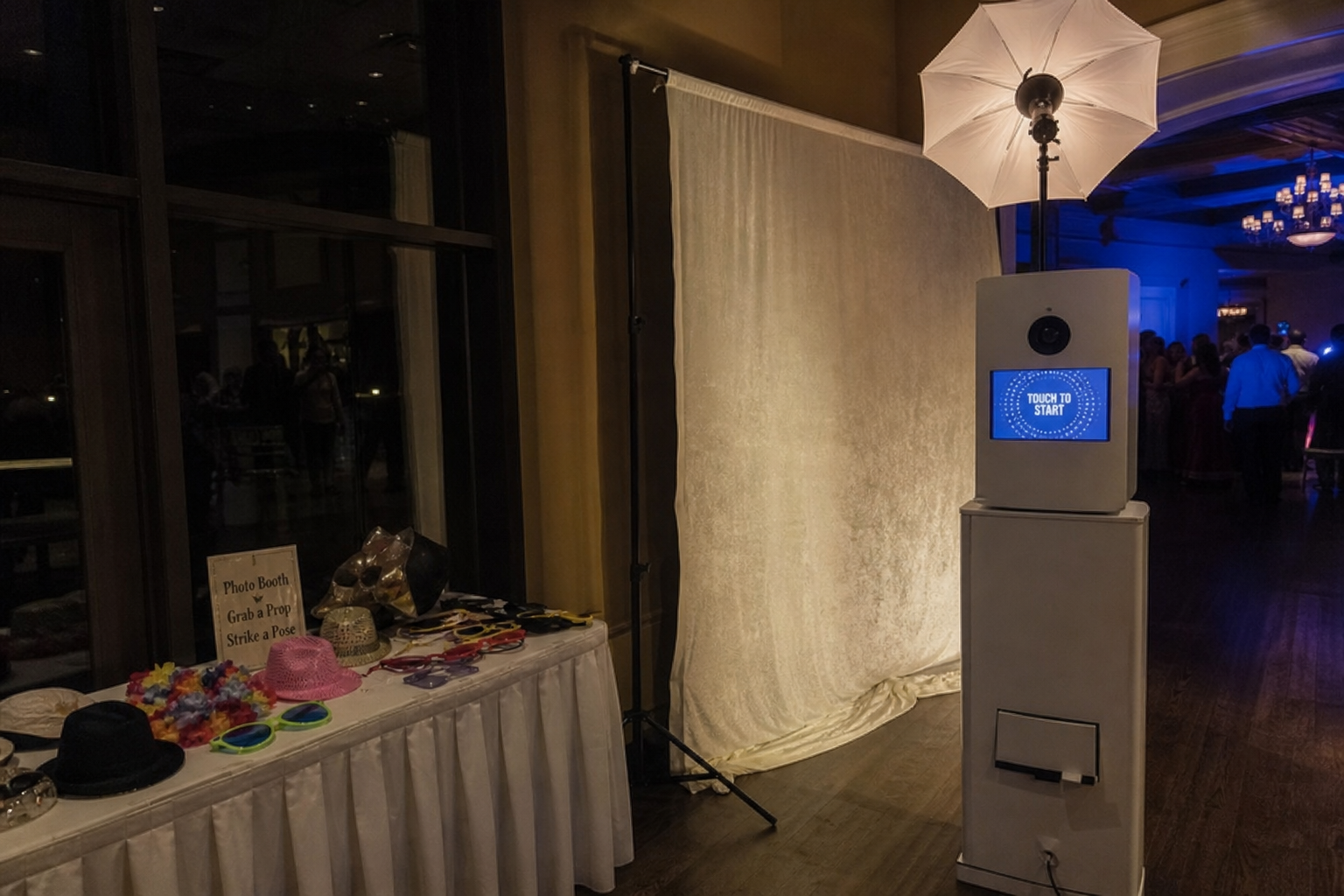 A photo booth station at a reception. The output is posed portraits, not candid moments. A wedding photo booth station with a black backdrop, props, and an attendant at a reception venue