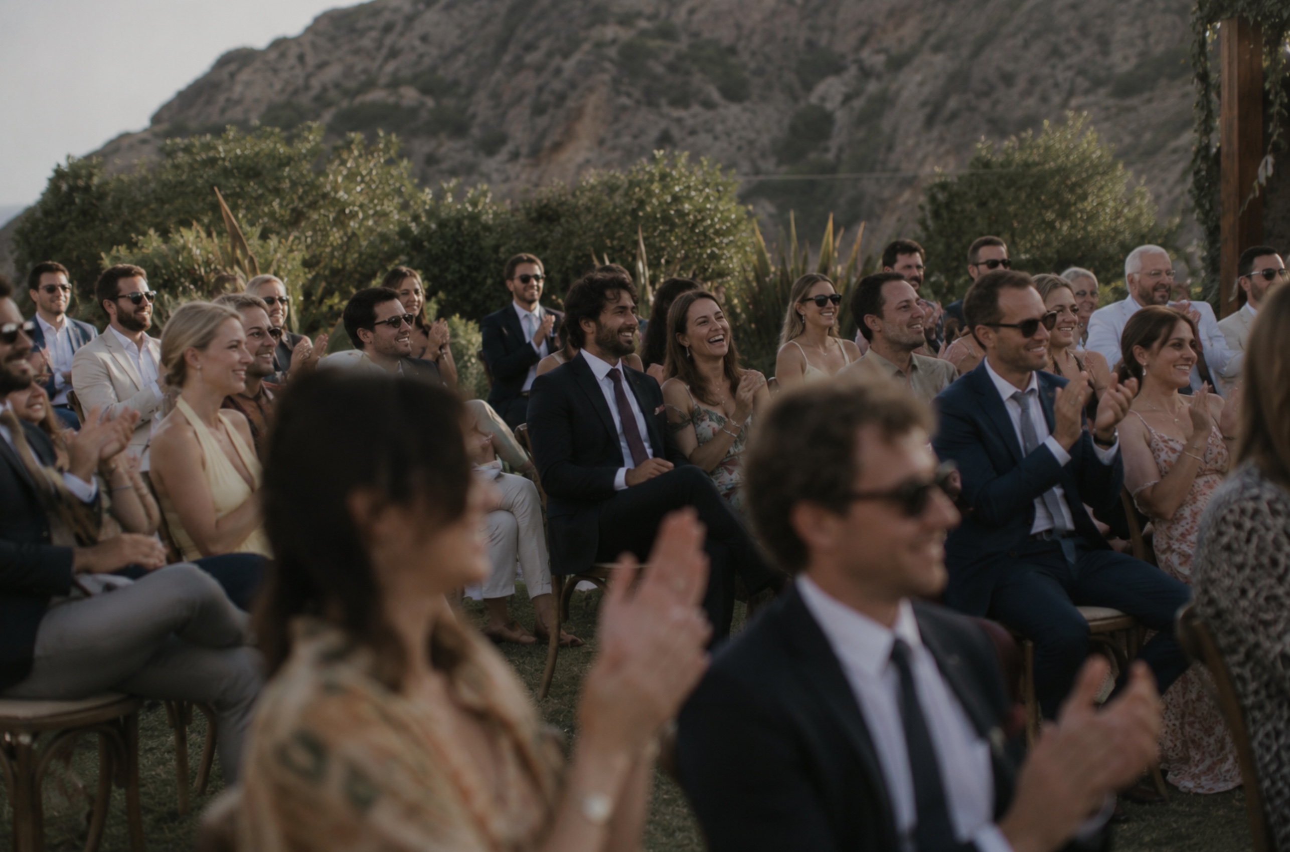 Wedding guests seated outdoors laughing and clapping during a reception